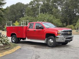 A red 2015 Chevrolet Silverado 3500HD truck with a utility bed featuring storage compartments and a sturdy body designed for heavy-duty tasks