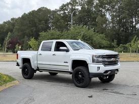 A white 2017 Chevrolet Silverado 1500 with black wheels parked at an angle showcasing its rugged design and elevated stance