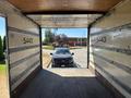 A 2022 Isuzu NQR truck viewed from inside its cargo area looking out towards a parking lot with another vehicle parked outside