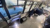 A 2021 Ford Transit van is parked with its blue exterior visible through large windows of the bus, showcasing a spacious interior with blue and gray seating options