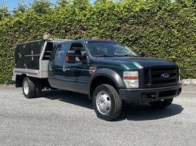 A green 2008 Ford F-550 utility truck with a flatbed and black toolboxes on the side, featuring large tires and a sturdy build