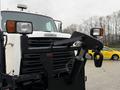 A 2016 Freightliner 108SD front view featuring a plow attachment and headlights with a yellow taxi in the distance