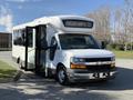 A white 2017 Chevrolet Express shuttle bus with an open front door and large windows stands parked on a street