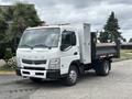 A white 2015 Mitsubishi Fuso FE160 with a flatbed and toolbox, featuring orange lights on the roof and a prominent front grille