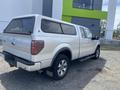 A silver 2014 Ford F-150 pickup truck with a camper shell and large tires parked in a lot