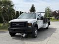 A white 2008 Ford F-550 with a black flatbed and orange lights on the roof is parked with its front facing the viewer