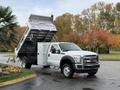 A white 2012 Ford F-550 dump truck is positioned with its bed raised, revealing the metal interior designed for transporting materials
