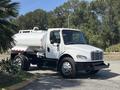 A white 2014 Freightliner M2 106 truck with a cylindrical tank on the back and chrome wheels parked on a road