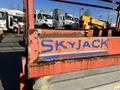 A red and blue SkyJack SJ lift with visible wear sits in the foreground showing the brand name prominently displayed on its side