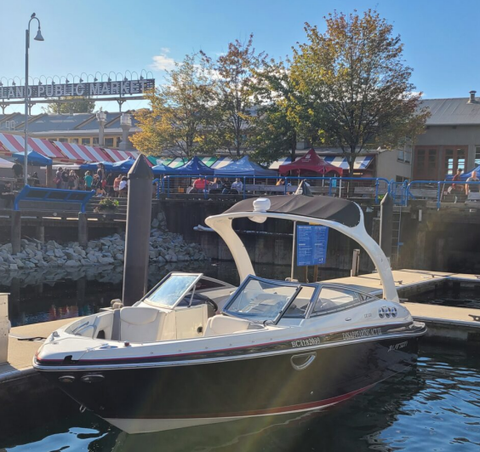 A black and white 2013 Larson 238 motorboat with a curved windshield and a bright blue bimini top docked at a marina