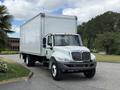 A 2022 International MV607 truck with a white box cargo area and a silver front grille is parked on a driveway with trees in the background