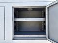 An empty compartment of a 2005 Freightliner M2 106 featuring a single metal shelf and multiple circular openings on the sides