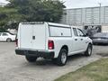 A white 2016 RAM 1500 pickup truck with a camper shell in the rear and black bumpers parked on a paved surface