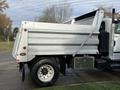 A silver 2011 International WorkStar dump truck with a raised bed and visible side panel features a standard rear tire and a storage compartment beneath the truck body
