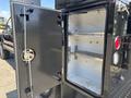 An open black storage compartment on the side of a 2022 Ford F-350 SD with shelves inside and a round lock on the door