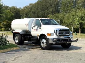 A white 2011 Ford F-750 fuel truck with a silver fuel tank and chrome wheels parked on a road