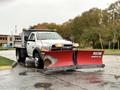 A 2012 Dodge Ram 5500 with a white body and red snow plow attached at the front positioned on a wet surface