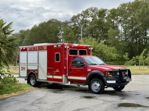 A red 2007 Ford F-550 fire rescue truck with a white compartment and emergency lights on top parked in a lot