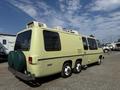 A vintage 1976 GMC Motorhome in yellow with a rear end featuring two green propane tanks and a distinctive aerodynamic shape