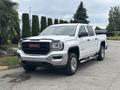 A white 2016 GMC Sierra 1500 pickup truck with chrome accents and black grille is parked on a road, featuring four doors and side steps.