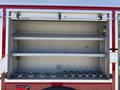 An open storage compartment of a 1991 International 4600 revealing two shelves with a row of metal fittings underneath