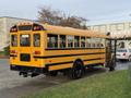 A yellow 2013 International 4300 school bus with an extended stop sign and black stripes on the side parked at an angle