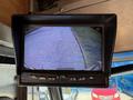 A monitor displaying a rearview camera feed showing a parking lot with visible outlines of vehicles and a clear path behind the camera