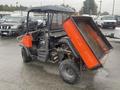 A 2010 Kubota RTV 900 utility vehicle with a dump bed set in the raised position showcasing its orange color and rugged design