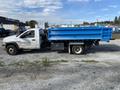 A 2009 Dodge Ram 5500 flatbed truck with a bright blue dump bed and white cab parked on gravel
