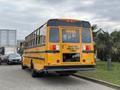A yellow 2022 Freightliner B2 school bus with large rear windows and emergency exit doors, displaying a warning sign about red lights flashing