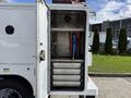 A 2024 Ford F-550 service truck with an open rear compartment featuring metal storage shelves and a mounted blue hose on a red reel