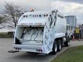 A white 2010 Autocar Xpeditor waste collection truck with a rear-loading compactor and multiple lights on the back