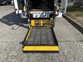 A black and yellow wheelchair ramp extended from the rear of a 2018 Ford Transit-350 with a textured surface and safety handles on either side
