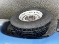 A mounted spare tire with a silver rim and a rugged black tread resting on a blue vehicle body
