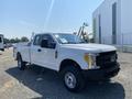 A white 2017 Ford F-250 Super Duty pickup truck with a flatbed and a crew cab parked on a gravel surface