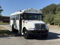 A 2013 International CE300 school bus in white with a black front bumper and large windows parked on a road