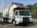 A 2011 Autocar Xpeditor garbage truck with a front-loading mechanism and a white body featuring green and blue stripes