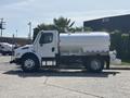 A 2014 Freightliner M2 106 water tanker truck with a shiny silver tank and black wheels parked on a pavement