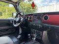 Interior of a 2021 Jeep Wrangler featuring a dashboard with touchscreen display steering wheel gear shift and red accents