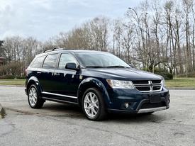 A blue 2013 Dodge Journey with silver alloy wheels parked at an intersection showcasing its sleek design and spacious SUV features