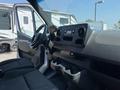 Interior of a 2022 Mercedes-Benz Sprinter featuring a dashboard with audio controls and cup holders as well as a steering wheel and seats visible