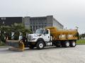 A 2016 International 7600 truck with a yellow snow plow attached in the front and a large bed for carrying materials in the back