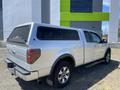 A silver 2014 Ford F-150 with a truck bed cap parked on gravel showing its side and rear features