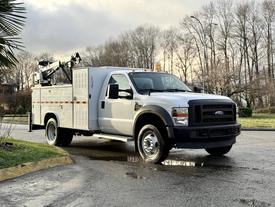 A 2010 Ford F-550 truck with a service body and utility equipment mounted on the back parked on a road