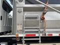 A silver 2013 Freightliner 114SD truck with a metal ladder and a strap securing the rear compartment featuring various labels and a warning sign