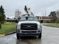 A 2012 Ford F-450 SD with a bucket lift attached on top facing forward with a white and black color scheme