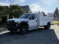 A 2009 Ford F-550 utility truck with a white exterior and service body featuring various compartments and amber lights
