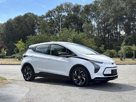 A 2023 Chevrolet Bolt EV in white parked on a street with trees in the background