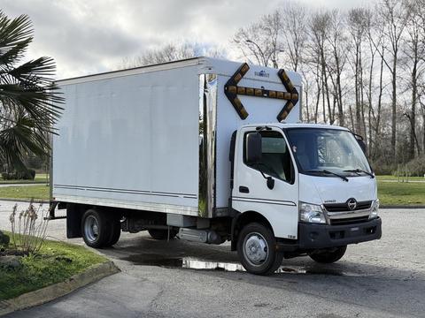 A 2014 Hino 195 box truck with a white body and chrome accents parked on a paved area