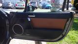 The interior door panel of a 2007 Mazda Miata featuring a black and brown color scheme with a circular speaker and a round cup holder